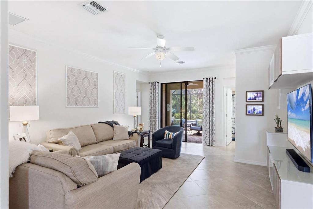 A bright living room features a beige sofa, dark blue armchair, and sliding glass patio doors — 20930 VALORE COURT, VENICE, FL