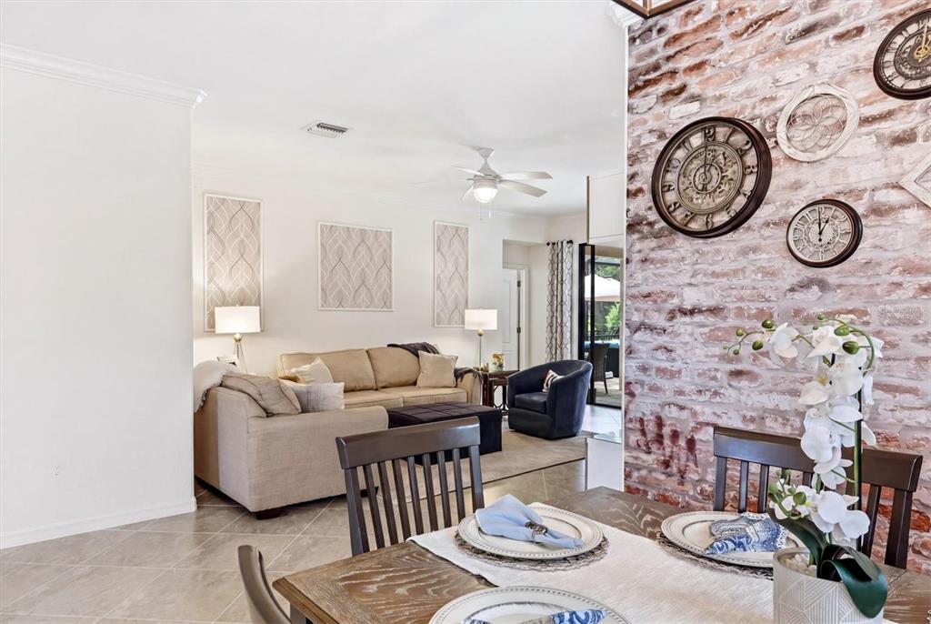 A dining area with a brick wall and clocks opens into a living room — 20930 VALORE COURT, VENICE, FL