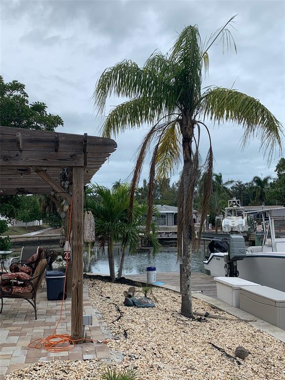 A palm tree stands on a gravel yard next to a wooden pergola and canal — 10004 CORTEZ ROAD W UNIT 102, BRADENTON, FL