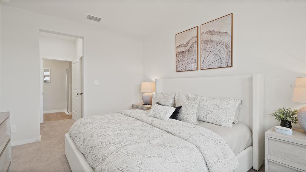 A bedroom features a white upholstered bed, patterned bedding, and wall art above the headboard — 5359 WHISPERING GARDEN WAY, CLERMONT, FL