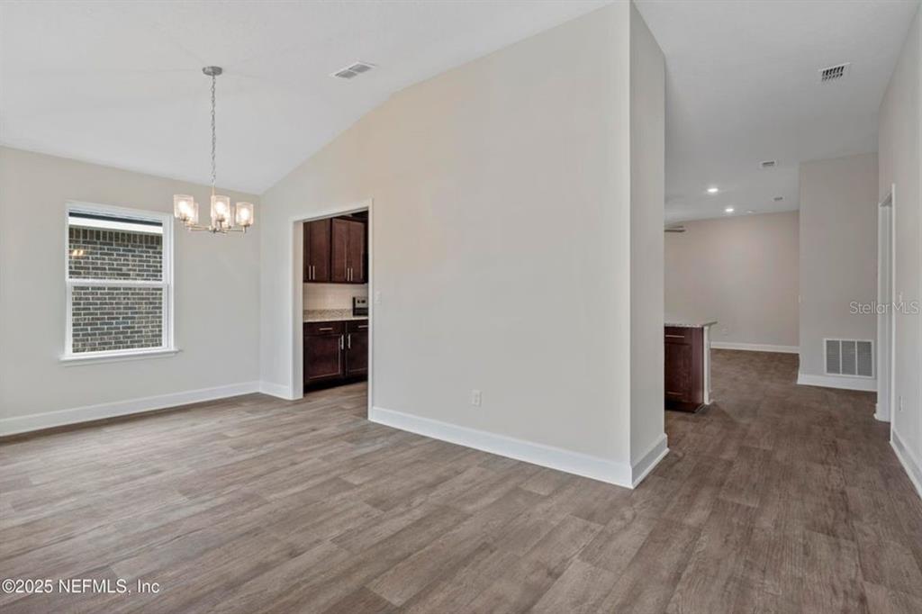 A dining area with a vaulted ceiling, chandelier, and wood-look flooring leads to a kitchen — 129 PRITCHARD DRIVE, PALM COAST, FL