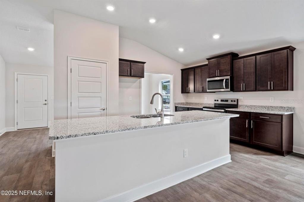 A kitchen features dark wood cabinets, granite countertops, a central island, and light flooring — 129 PRITCHARD DRIVE, PALM COAST, FL