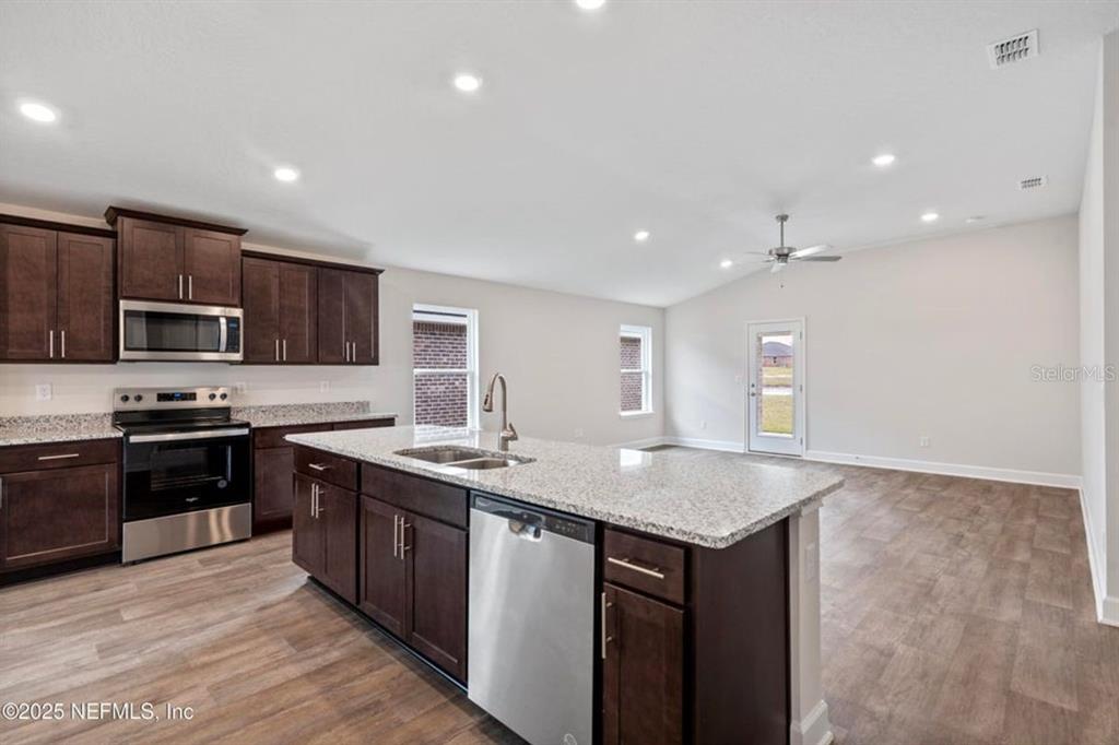 A kitchen with dark wood cabinets, granite countertops, and stainless steel appliances opens to a living area — 129 PRITCHARD DRIVE, PALM COAST, FL