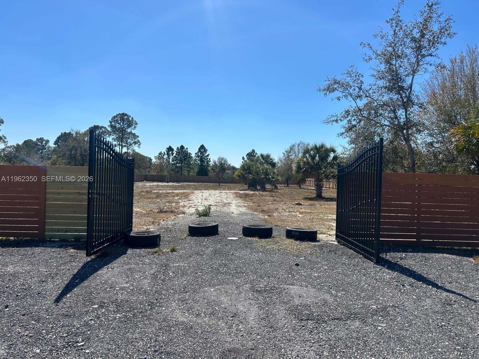 An open black metal gate leads to a gravel driveway on a vacant lot — 648 Hunting Club Ave, Clewiston FL 33440, CLEWISTON, FL