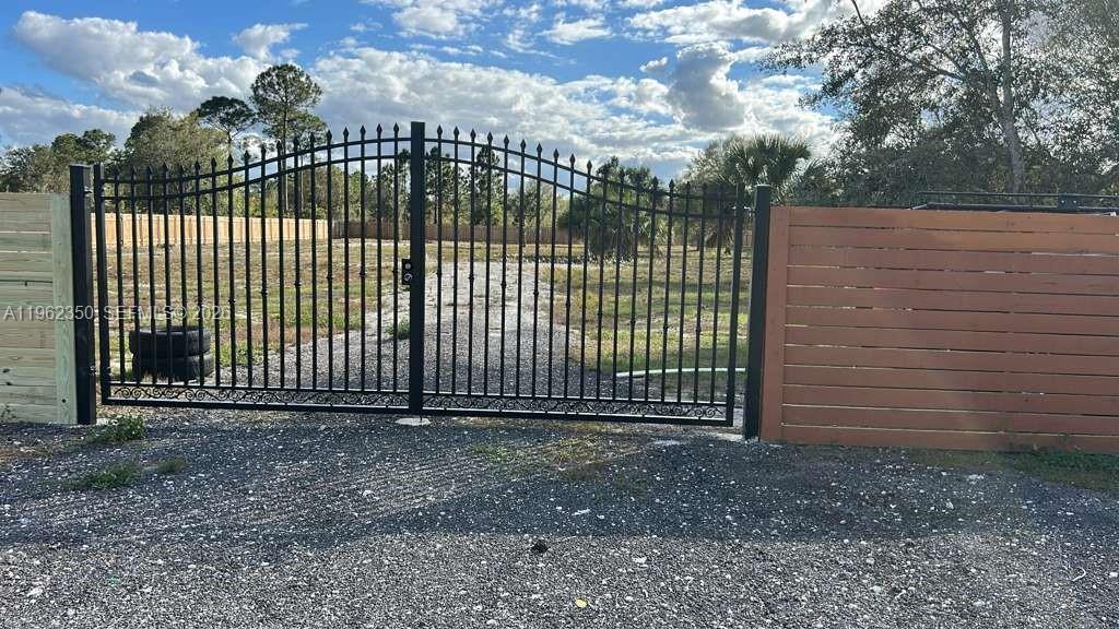 A black metal gate stands between two wooden fences at the entrance to a lot — 648 Hunting Club Ave, Clewiston FL 33440, CLEWISTON, FL