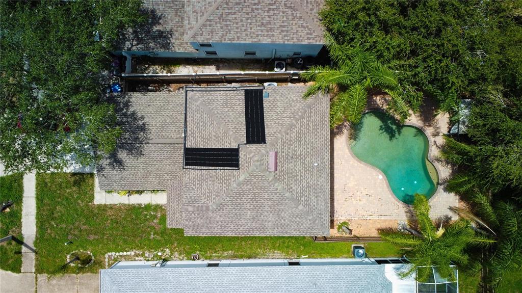 An aerial view shows a house roof with solar panels, a pool, and surrounding landscaping — 10468 BLACKMORE DRIVE, TAMPA, FL