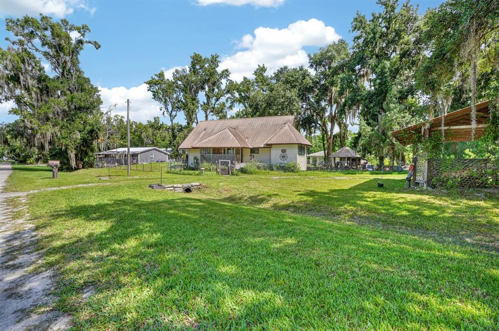 A tan house with a metal roof sits on a large, grassy lot with trees — 110 W PALM AVENUE, CRESCENT CITY, FL