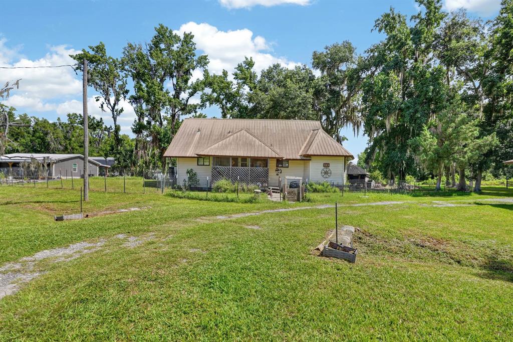 A one-story house with a metal roof sits on a grassy lot with trees — 110 W PALM AVENUE, CRESCENT CITY, FL
