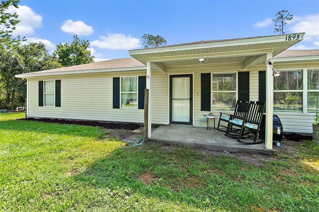 A single-story house with light siding, a covered front porch, and two rocking chairs — 1893 WATER OAK ROAD, BUNNELL, FL