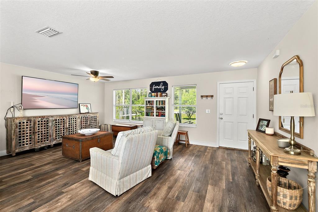 A living room features wood-look flooring, a large television, a wooden console, and a white door — 1893 WATER OAK ROAD, BUNNELL, FL