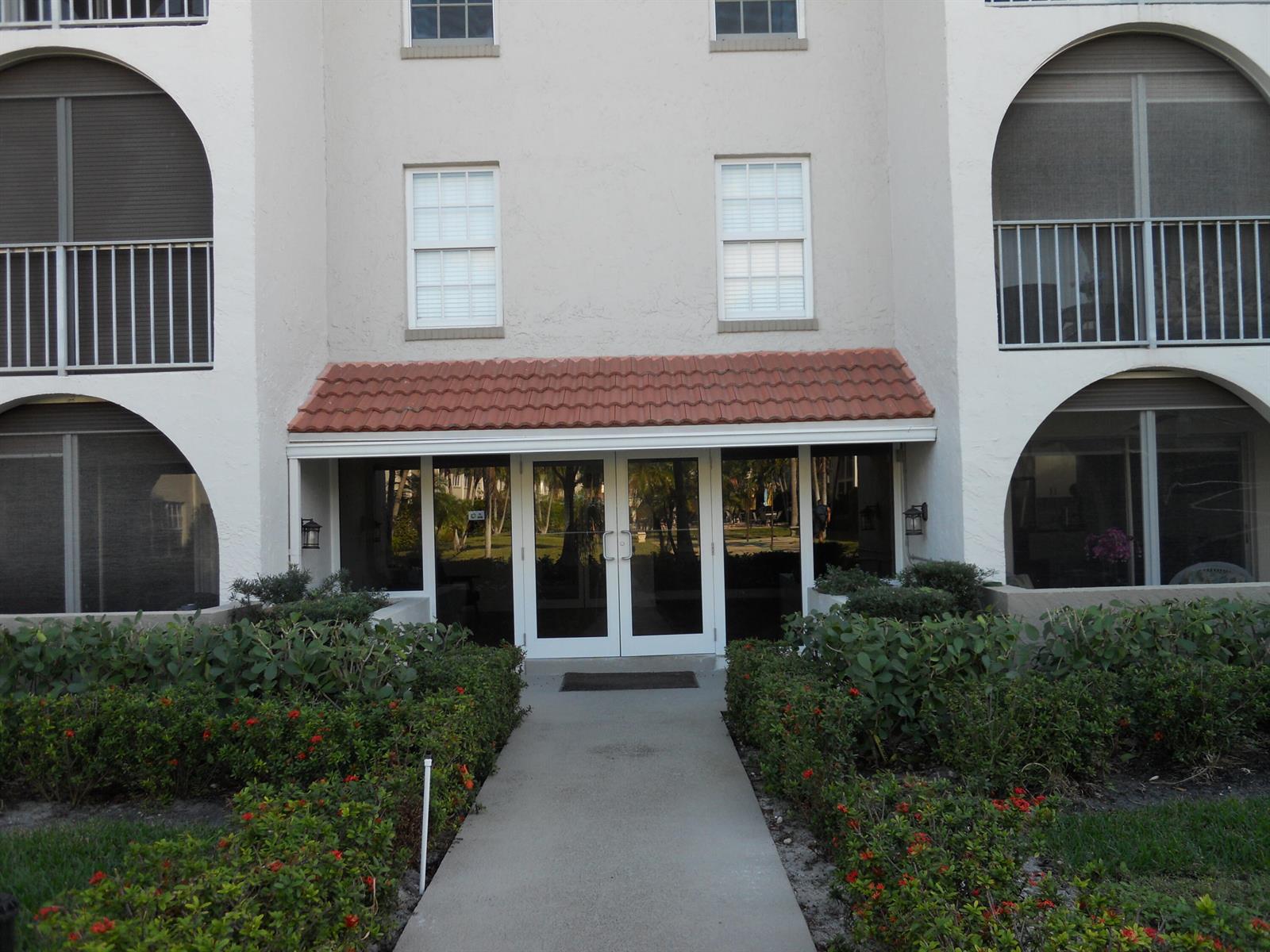 A concrete walkway leads to the glass double-door entrance of a multi-story residential building — 250 NE 20th Street # 123s, Boca Raton FL 33431, BOCA RATON, FL