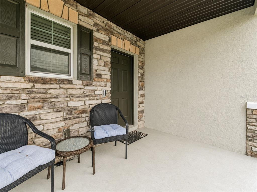 A covered porch features stone veneer siding, a dark door, and two wicker chairs — 7840 ABBY BROOKS CIRCLE, WESLEY CHAPEL, FL