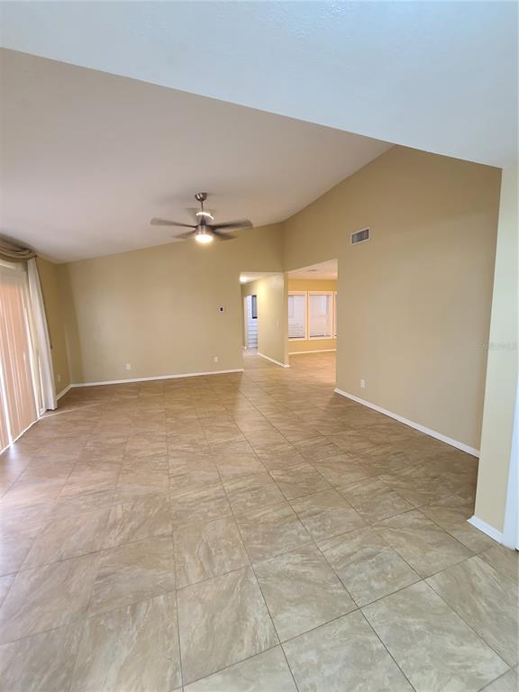 An empty living room with vaulted ceilings, beige walls, and large tan floor tiles — 13701 LAZY OAK DRIVE, TAMPA, FL