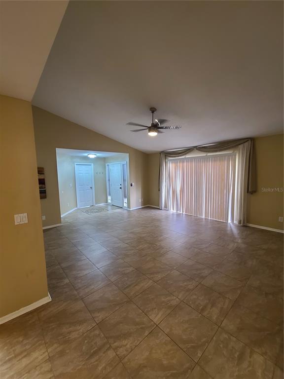 A spacious living room features light-colored tile flooring, a vaulted ceiling, and sliding glass doors — 13701 LAZY OAK DRIVE, TAMPA, FL
