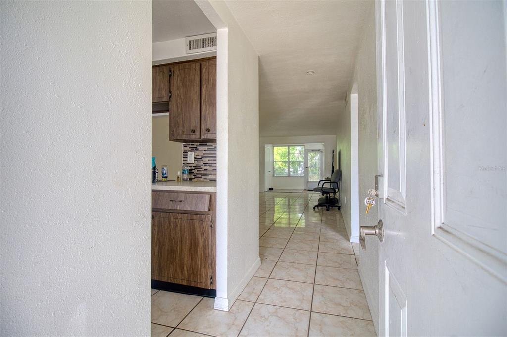 A view from an open doorway into a tiled hallway leading to a kitchen and living area — 4242 REDCLIFF PLACE UNIT C, NEW PORT RICHEY, FL