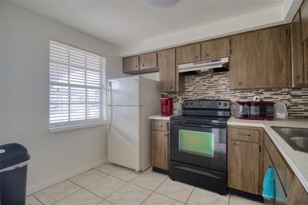 A kitchen with wood cabinets, black appliances, a tiled backsplash, and a window — 4242 REDCLIFF PLACE UNIT C, NEW PORT RICHEY, FL