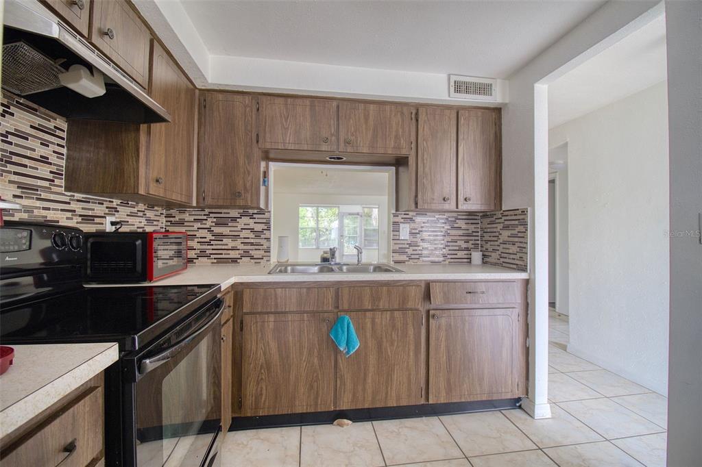 A kitchen with wood-grain cabinets, a mosaic tile backsplash, and a pass-through window — 4242 REDCLIFF PLACE UNIT C, NEW PORT RICHEY, FL