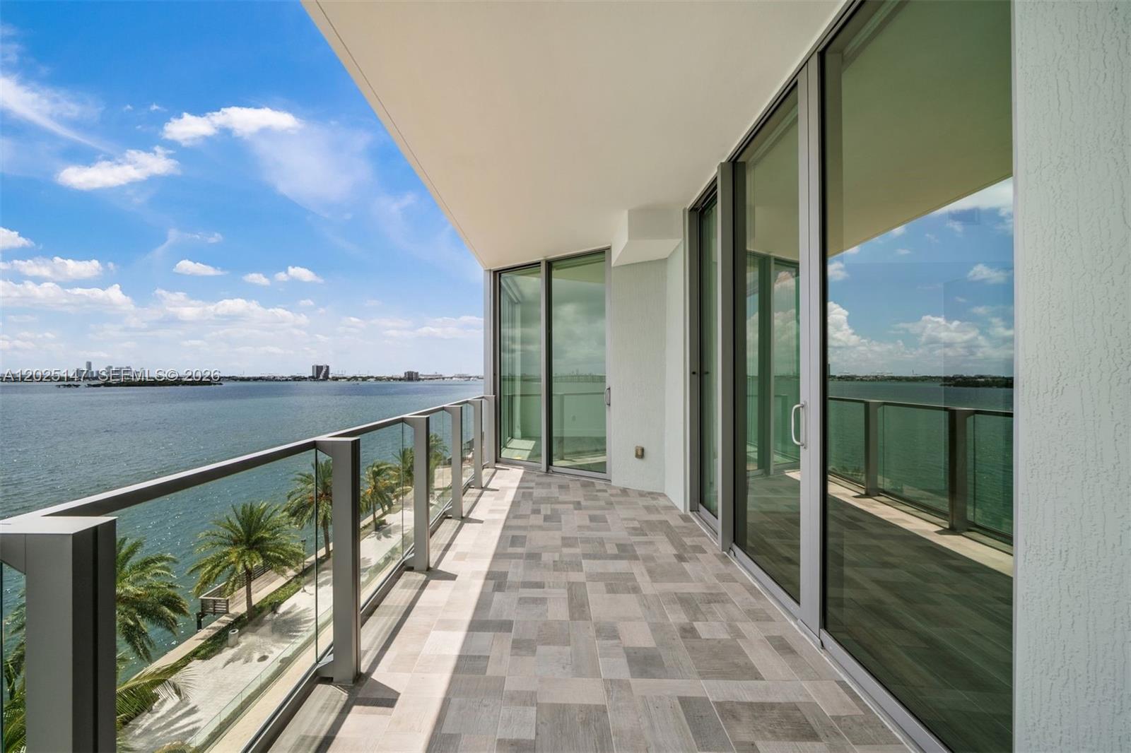 A balcony with glass railings overlooks the water, featuring tiled flooring and sliding glass doors — 2900 NE 7th Ave # 504, Miami FL 33137, MIAMI, FL