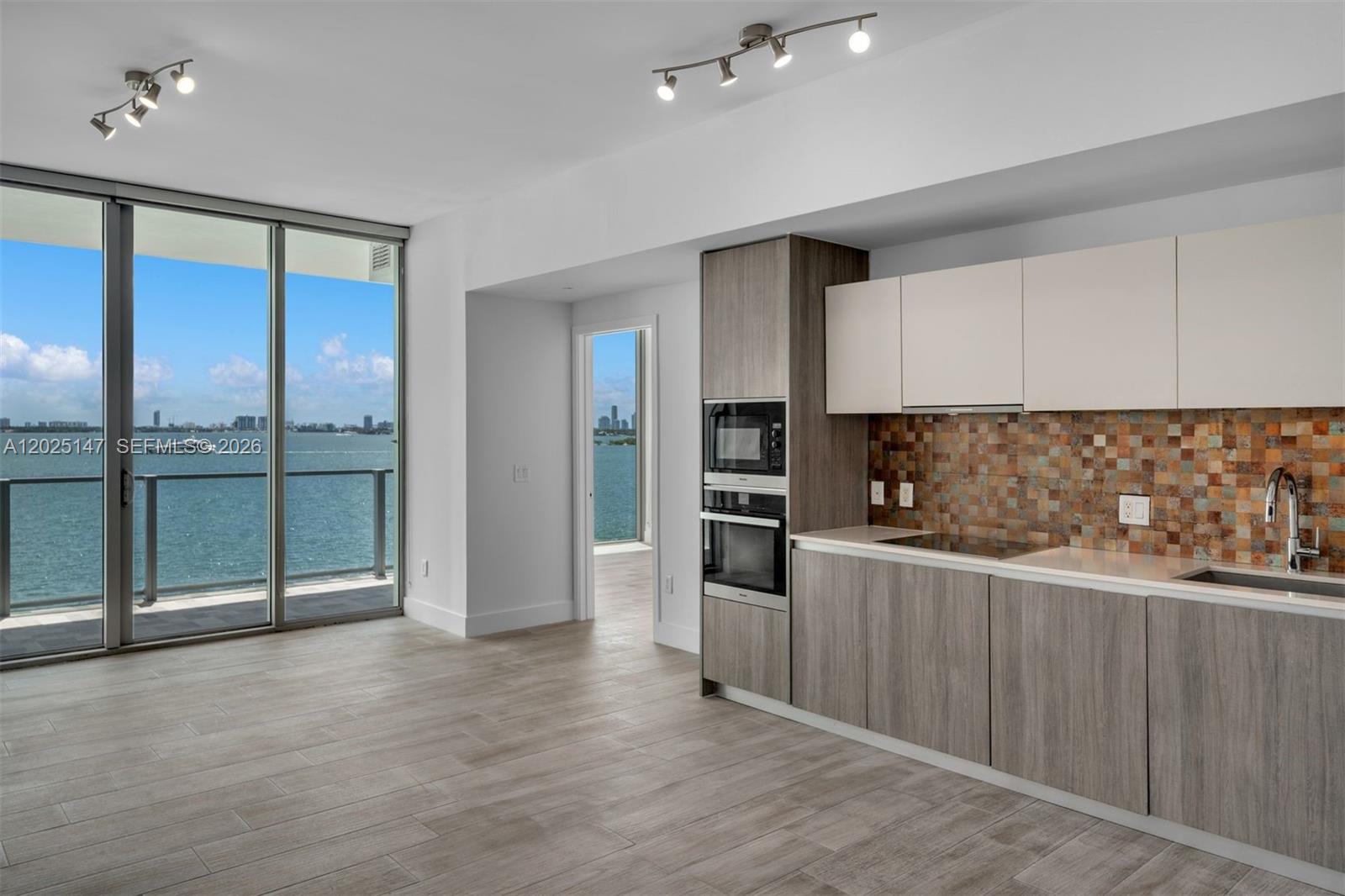 A modern kitchen with wood-toned cabinets and a mosaic backsplash overlooks a waterfront balcony — 2900 NE 7th Ave # 504, Miami FL 33137, MIAMI, FL
