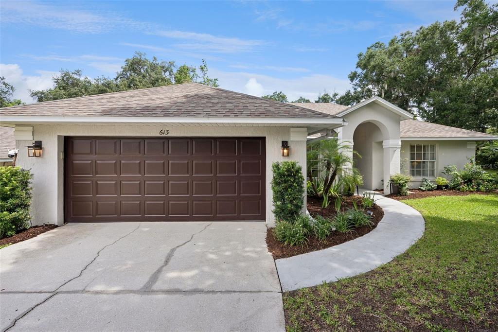 A single-story house with a brown garage door, arched entryway, and a concrete driveway — 613 HURON PLACE, MOUNT DORA, FL