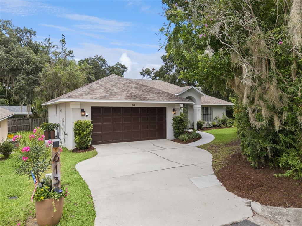 A single-story house with a brown garage door, a concrete driveway, and surrounding trees — 613 HURON PLACE, MOUNT DORA, FL