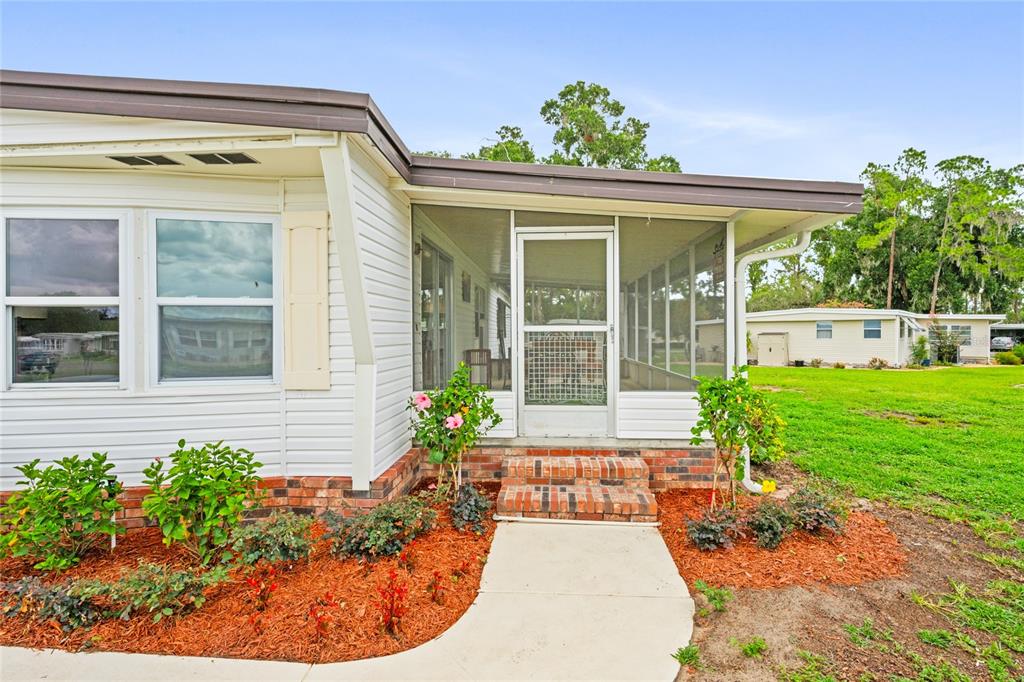 A white mobile home features a screened-in porch with brick steps and landscaped mulch beds — 150 AZALEA TRAIL, LEESBURG, FL