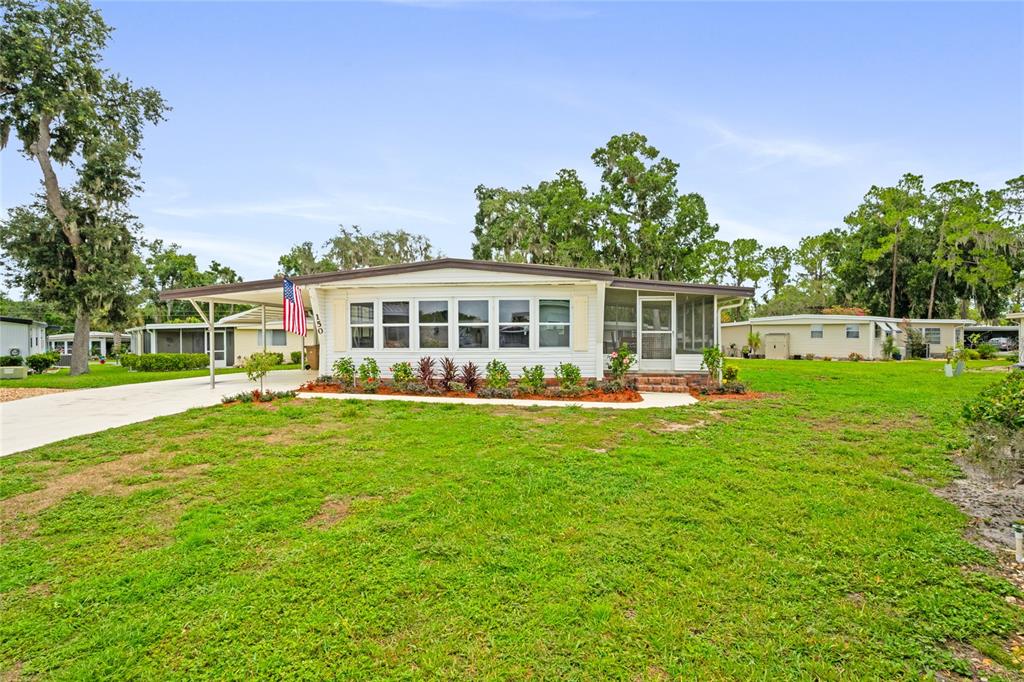 A single-story manufactured home with a carport, front porch, and a large grassy yard — 150 AZALEA TRAIL, LEESBURG, FL