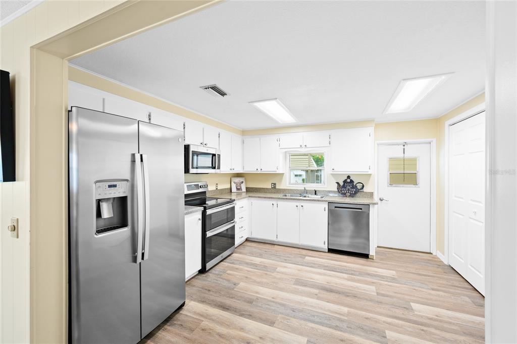 A kitchen with white cabinets, stainless steel appliances, and wood-look flooring — 150 AZALEA TRAIL, LEESBURG, FL