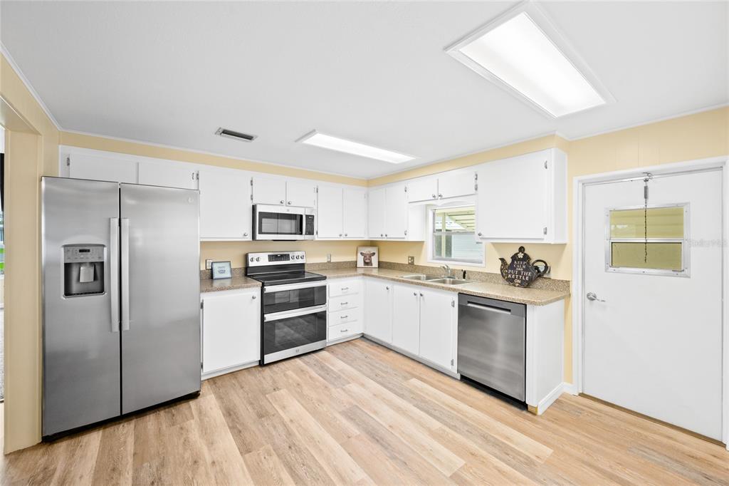 A kitchen features white cabinets, stainless steel appliances, light countertops, and wood-look flooring — 150 AZALEA TRAIL, LEESBURG, FL