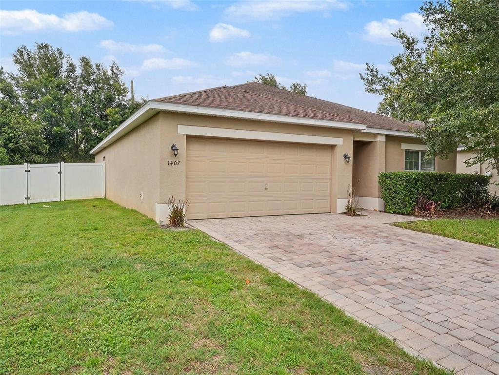 A single-story house with a beige stucco exterior, a two-car garage, and a paver driveway — 1407 MARSH MEADOW LN, DAVENPORT, FL