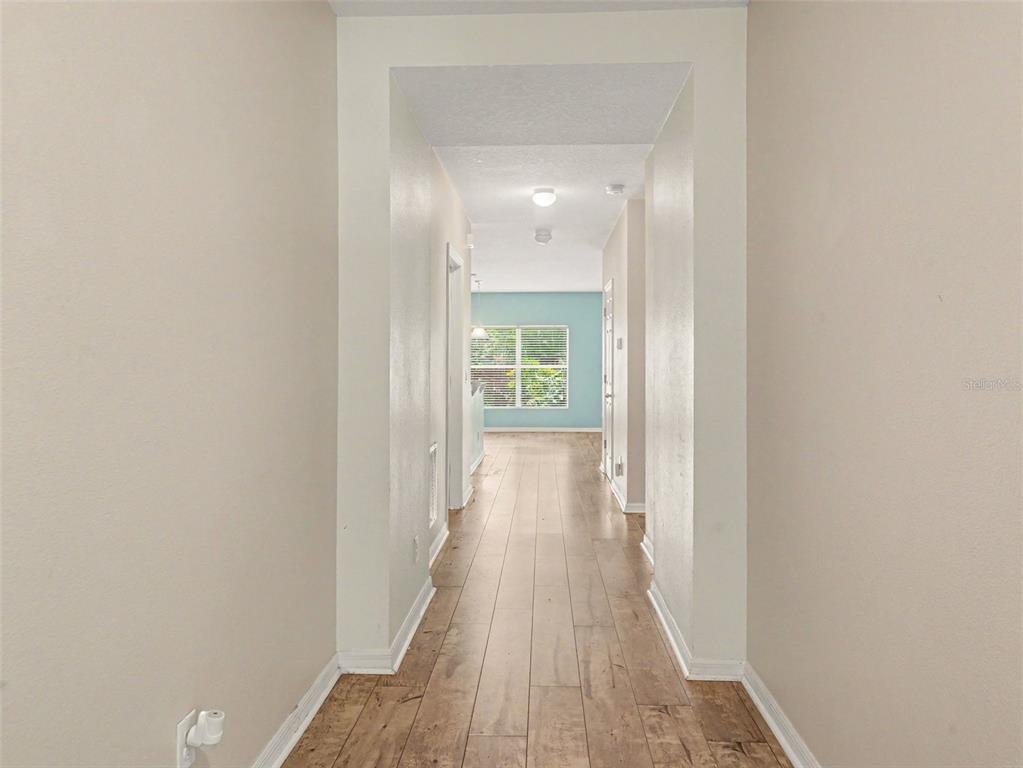 A hallway with light wood-look flooring leads to a room with a light blue wall — 1407 MARSH MEADOW LN, DAVENPORT, FL