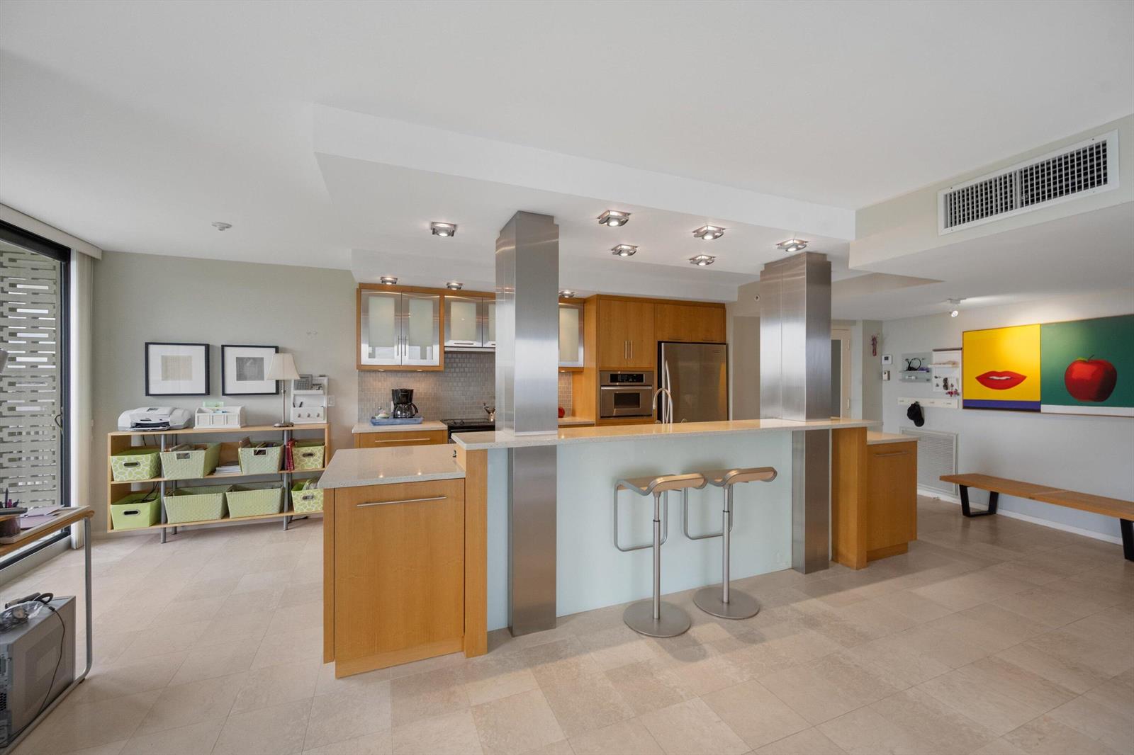 A modern kitchen features light wood cabinets, stainless steel columns, and a breakfast bar — 3360 S Ocean Boulevard # I, Palm Beach FL 33480, PALM BEACH, FL