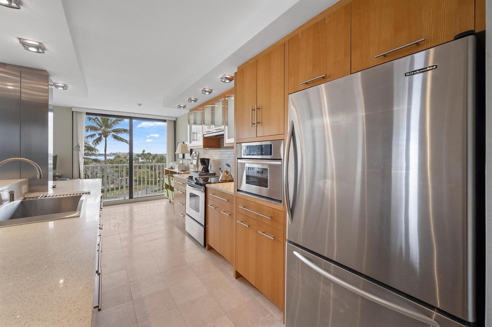 A modern kitchen features light wood cabinets, stainless steel appliances, and a view of palm trees — 3360 S Ocean Boulevard # I, Palm Beach FL 33480, PALM BEACH, FL