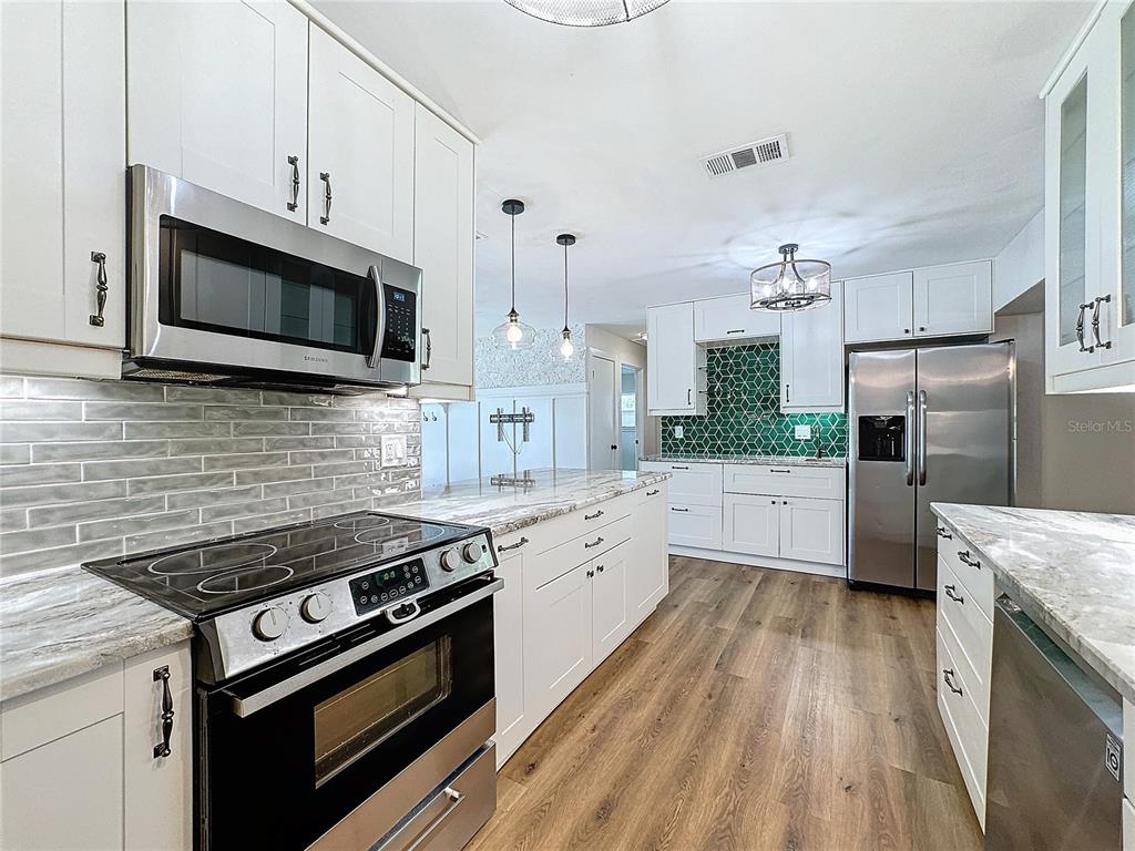 A kitchen features white cabinets, stainless steel appliances, a green tiled backsplash, and wood flooring — 7610 117TH STREET, SEMINOLE, FL