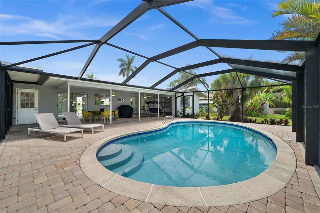 A screened-in patio features a kidney-shaped swimming pool, lounge chairs, and a dining area — 5122 SW 3RD AVENUE, CAPE CORAL, FL