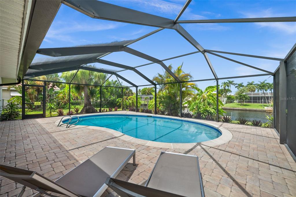 A screened-in pool patio features a kidney-shaped pool, paver flooring, and lounge chairs — 5122 SW 3RD AVENUE, CAPE CORAL, FL
