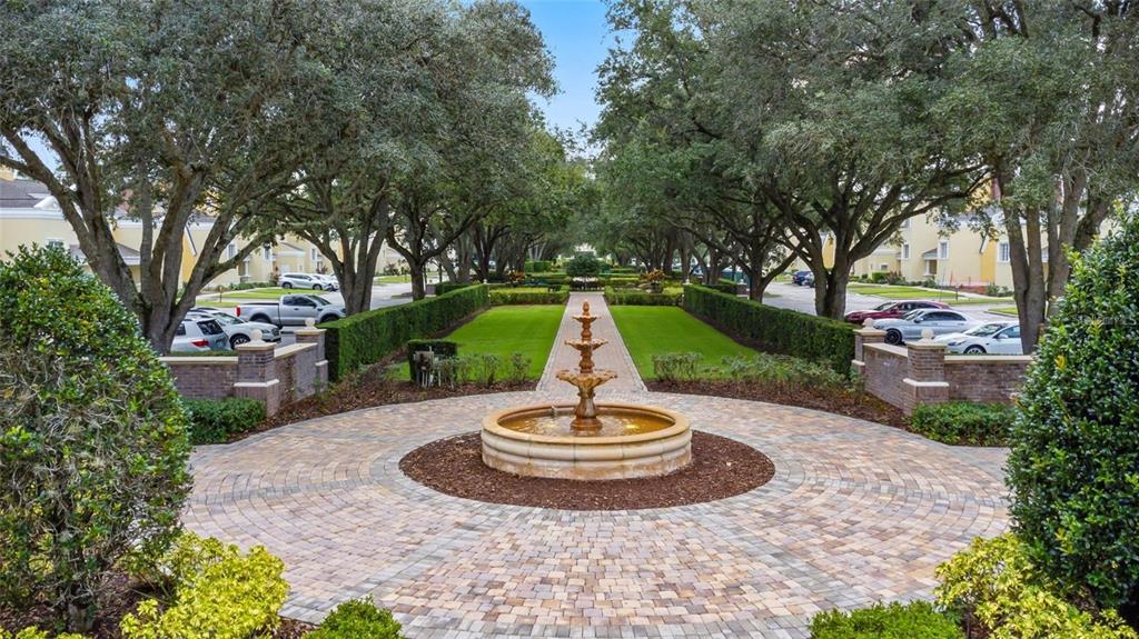 A stone fountain sits in the center of a circular brick courtyard lined with trees — 1342 SEVEN EAGLES COURT, REUNION, FL