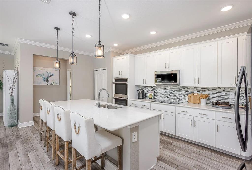 A kitchen features white cabinets, a large island with bar seating, and wood-look flooring — 21 SWEETBAY COURT E, HOMOSASSA, FL