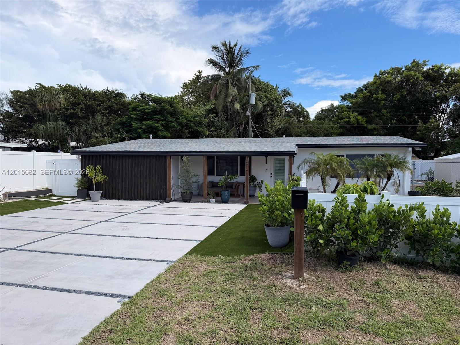 A single-story house features a concrete driveway, a covered porch, and a white fence — 310 NE 12th Ave, Pompano Beach FL 33060, POMPANO BEACH, FL