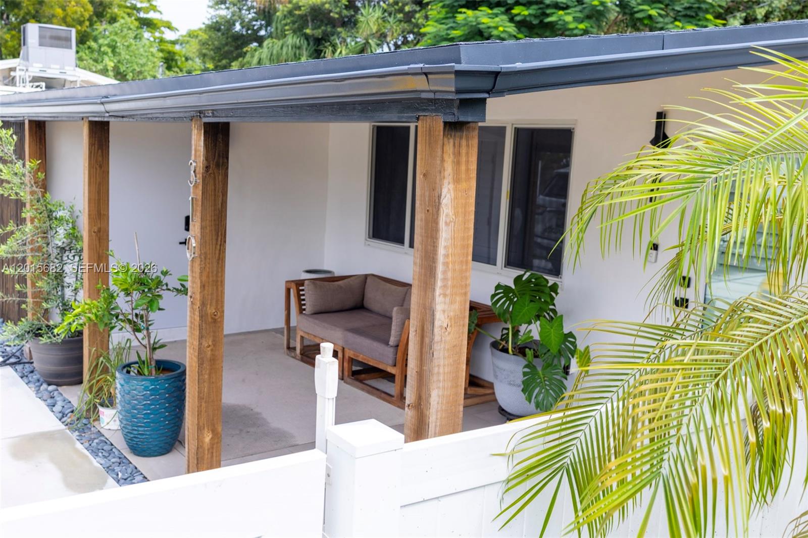 A covered patio features wooden support posts, a small sofa, and several potted plants — 310 NE 12th Ave, Pompano Beach FL 33060, POMPANO BEACH, FL