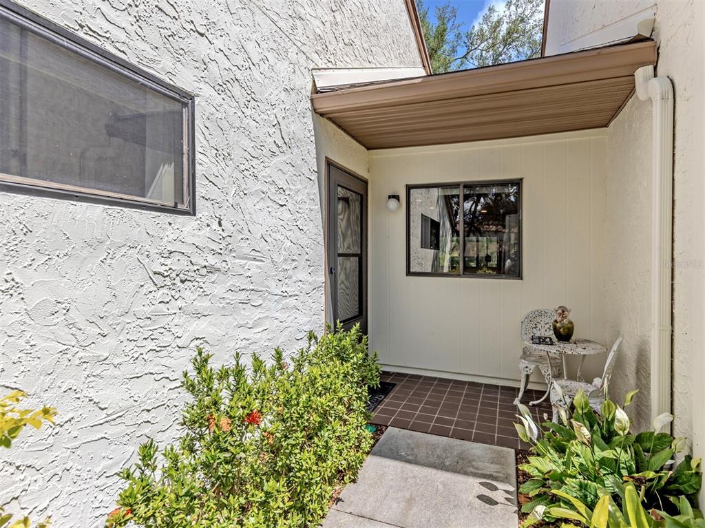 A covered entryway features a tiled floor, a glass-paneled door, and a small bistro set — 868 BIRD BAY WAY UNIT 197, VENICE, FL