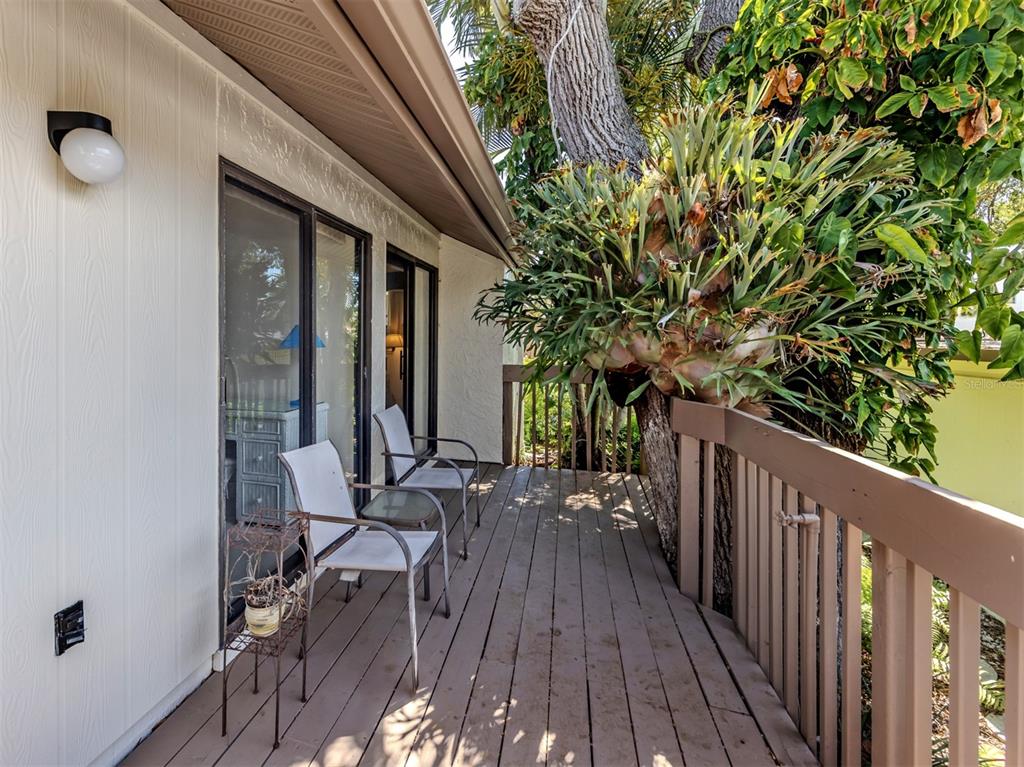 A wooden deck features two chairs, a small table, and a large staghorn fern plant — 868 BIRD BAY WAY UNIT 197, VENICE, FL