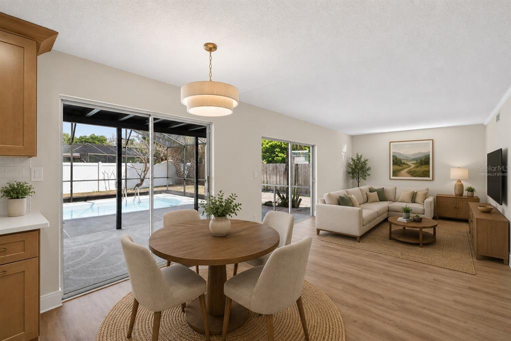 A dining area and living room with wood-look flooring overlook a patio and swimming pool — 180 FLORIDA BOULEVARD, MERRITT ISLAND, FL