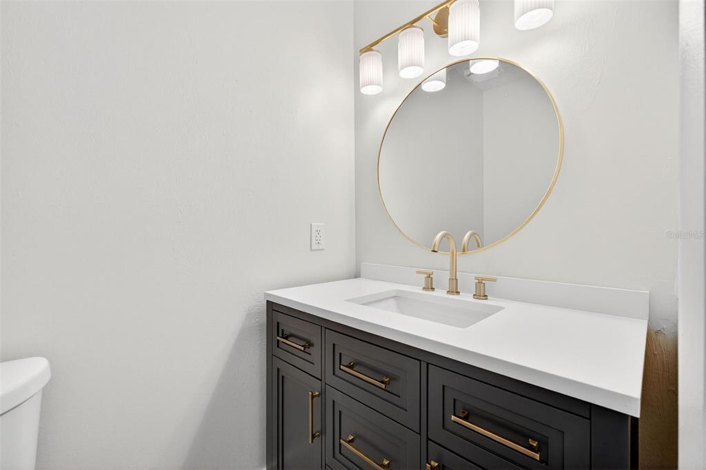 A bathroom features a dark vanity with gold hardware, a round mirror, and a light fixture — 180 FLORIDA BOULEVARD, MERRITT ISLAND, FL