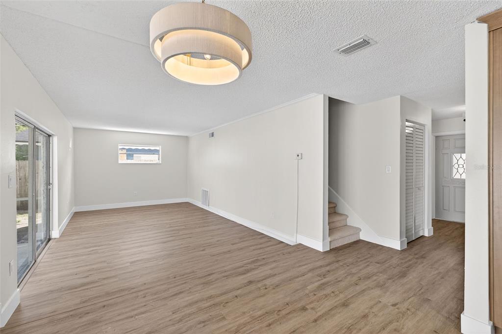 An empty living room features light wood flooring, a modern drum pendant light, and stairs — 180 FLORIDA BOULEVARD, MERRITT ISLAND, FL