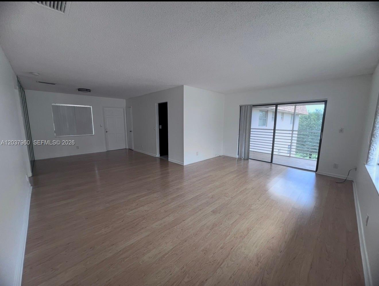 An empty living room features light wood-look flooring, white walls, and a sliding glass door — 2430 SW 81st Ave # 408, Davie FL 33324, DAVIE, FL