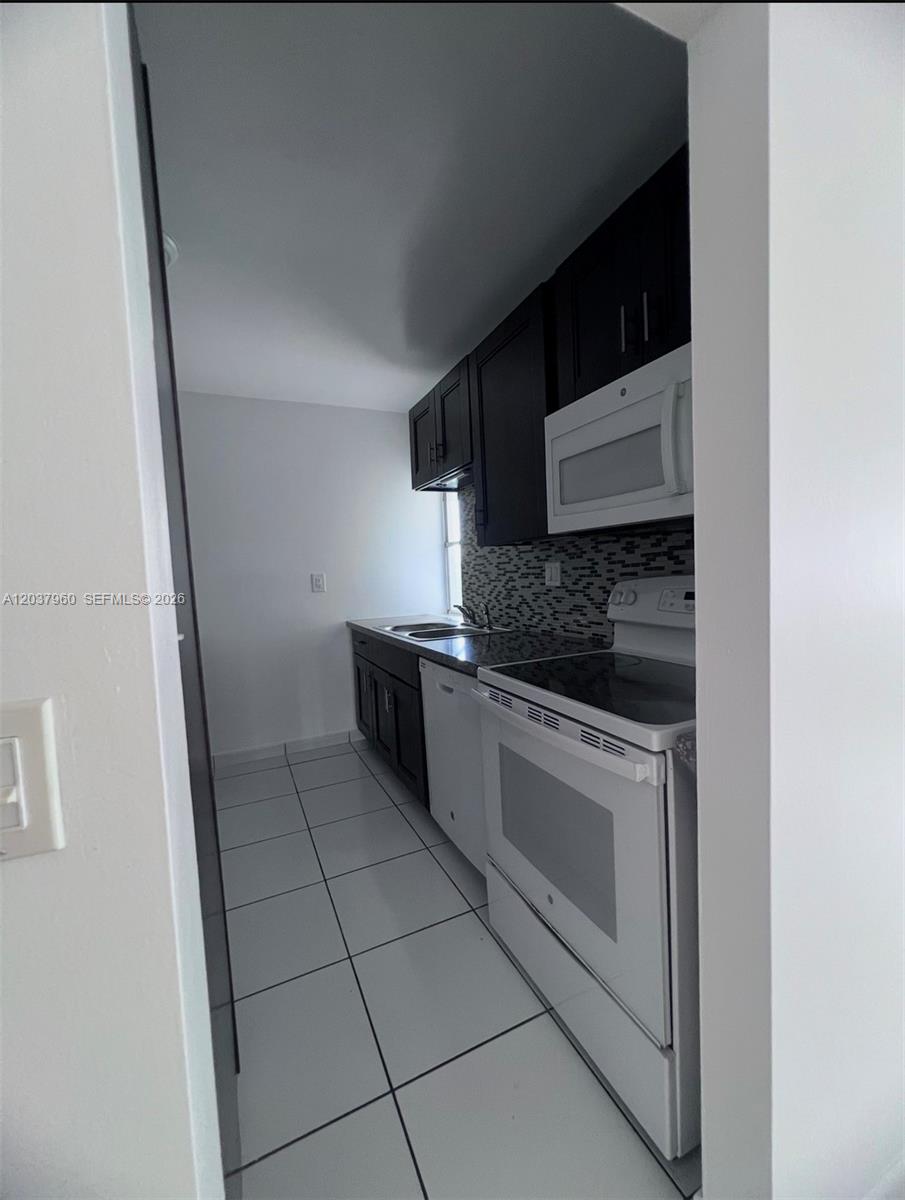 A galley-style kitchen features dark wood cabinets, white appliances, and a tiled floor — 2430 SW 81st Ave # 408, Davie FL 33324, DAVIE, FL