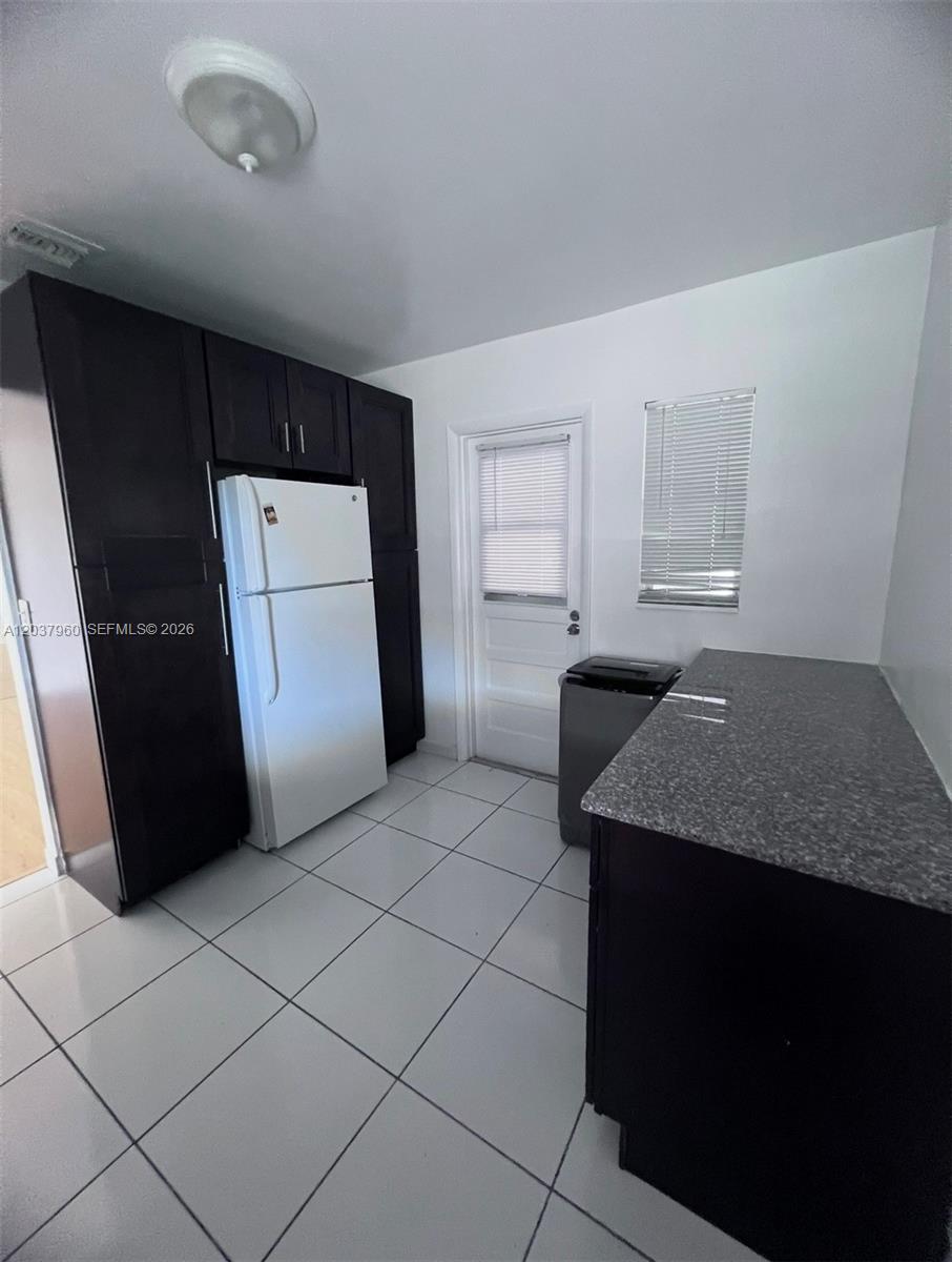 A kitchen features dark cabinets, a white refrigerator, a granite countertop, and tile flooring — 2430 SW 81st Ave # 408, Davie FL 33324, DAVIE, FL