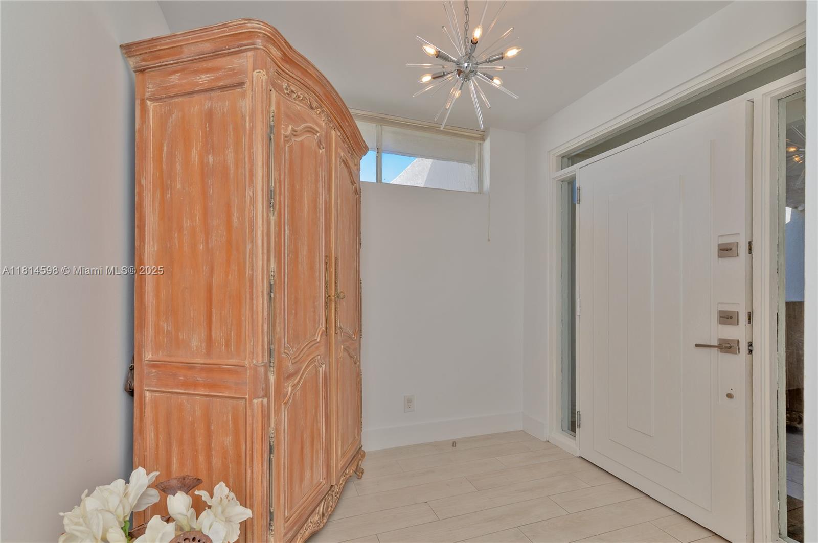 An entryway features a large wooden armoire, a modern sputnik chandelier, and a white door — 101 Crandon Blvd # 480, Key Biscayne FL 33149, KEY BISCAYNE, FL