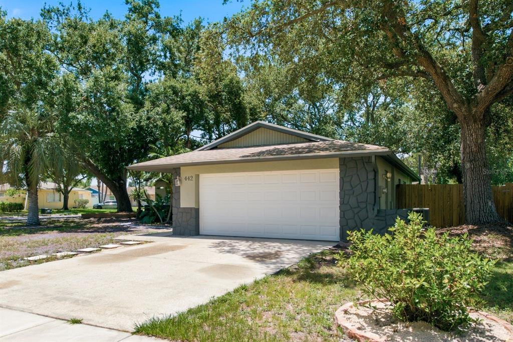 A detached garage with a white door and gray stone accents sits under large trees — 442 EVERGREEN DRIVE, OLDSMAR, FL